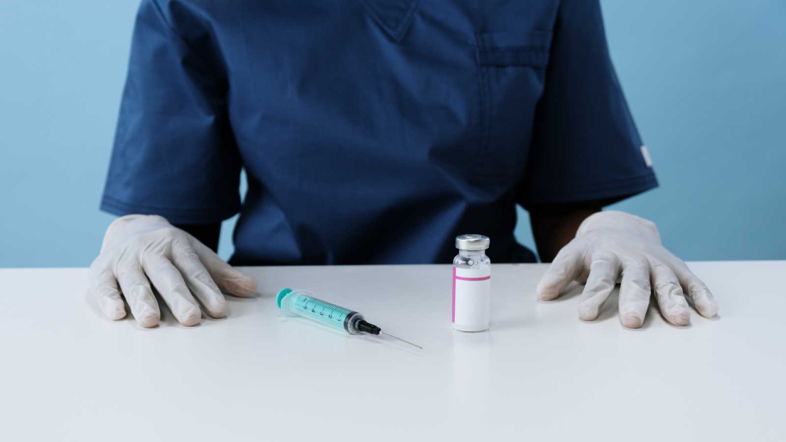 busto di medico seduto con davanti una siringa e una fiala di vaccino