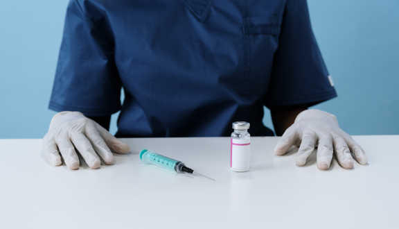 busto di medico seduto con davanti una siringa e una fiala di vaccino