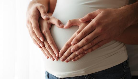 Le mani di un uomo appoggiate a quelle di una donna, a loro volte appoggiate alla pancia della donna ingrossata per la gravidanza