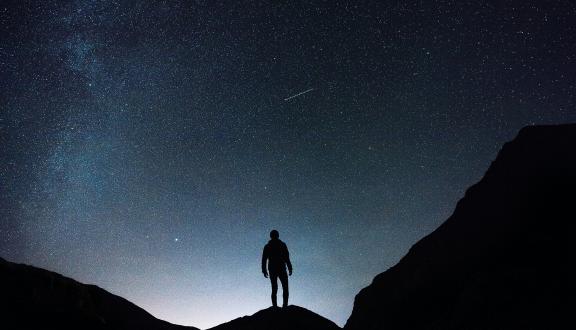 Silhouette di un uomo in un paesaggio di montagna di notte sullo sfondo del cielo stellato