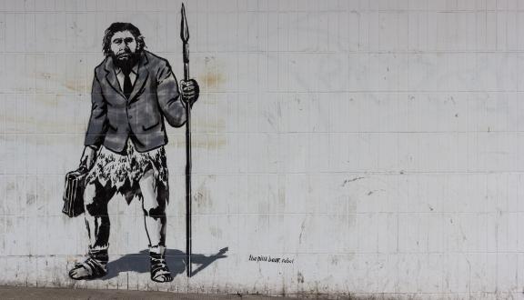 A primitive man with a spear, blazer and briefcase