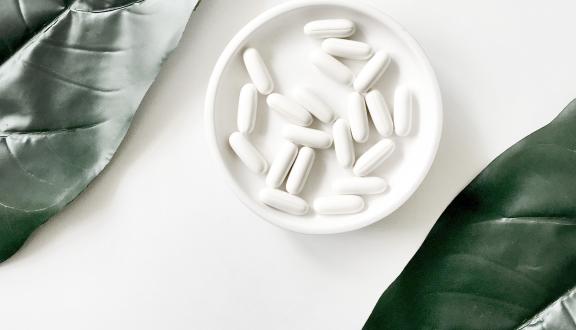 Un piattino pieno di compresse di un farmaco bianco tra due foglie verdi